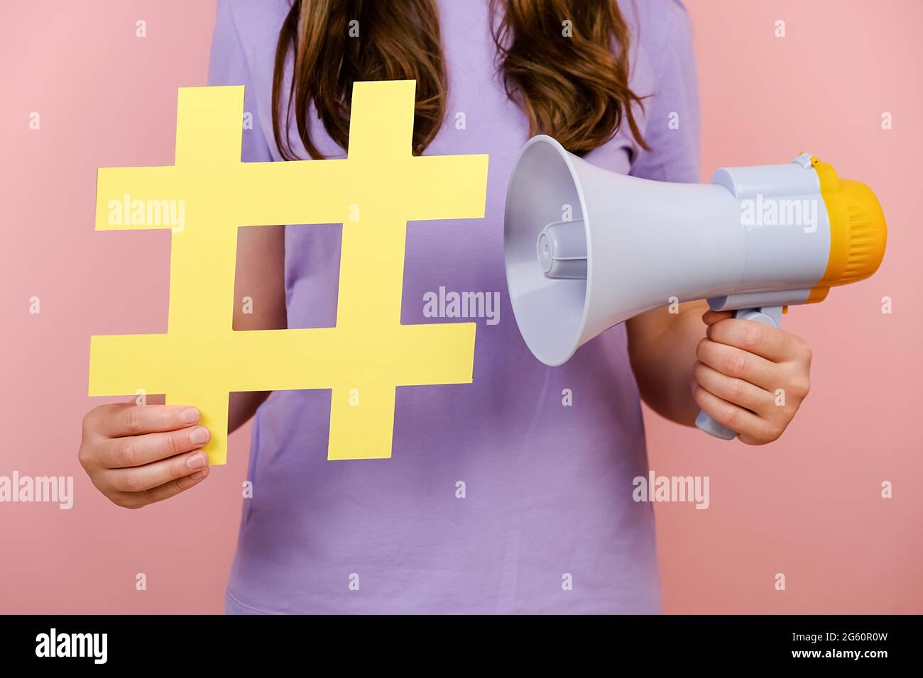 Gros plan petite femme écourtée tenant un panneau jaune hashtag et le mégaphone, étiquette pour les affaires, le marketing et la publicité, isolée sur fond rose Banque D'Images