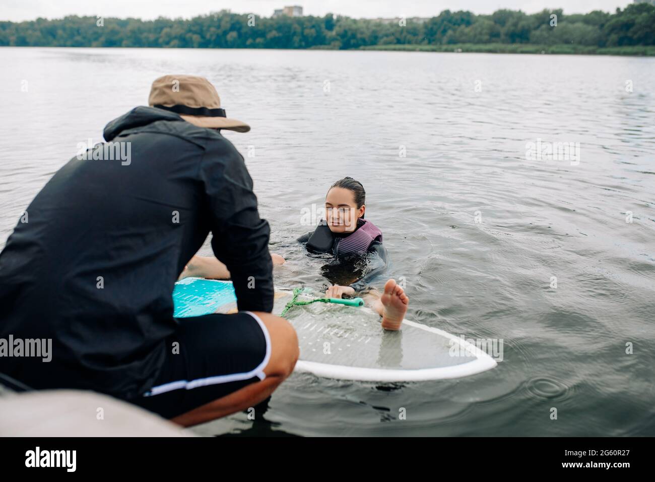 L'instructeur enseigne la technique de wakesurfing à une jeune femme et elle apprend à se tenir debout sur le surf tout en tenant à la corde de remorquage. Banque D'Images