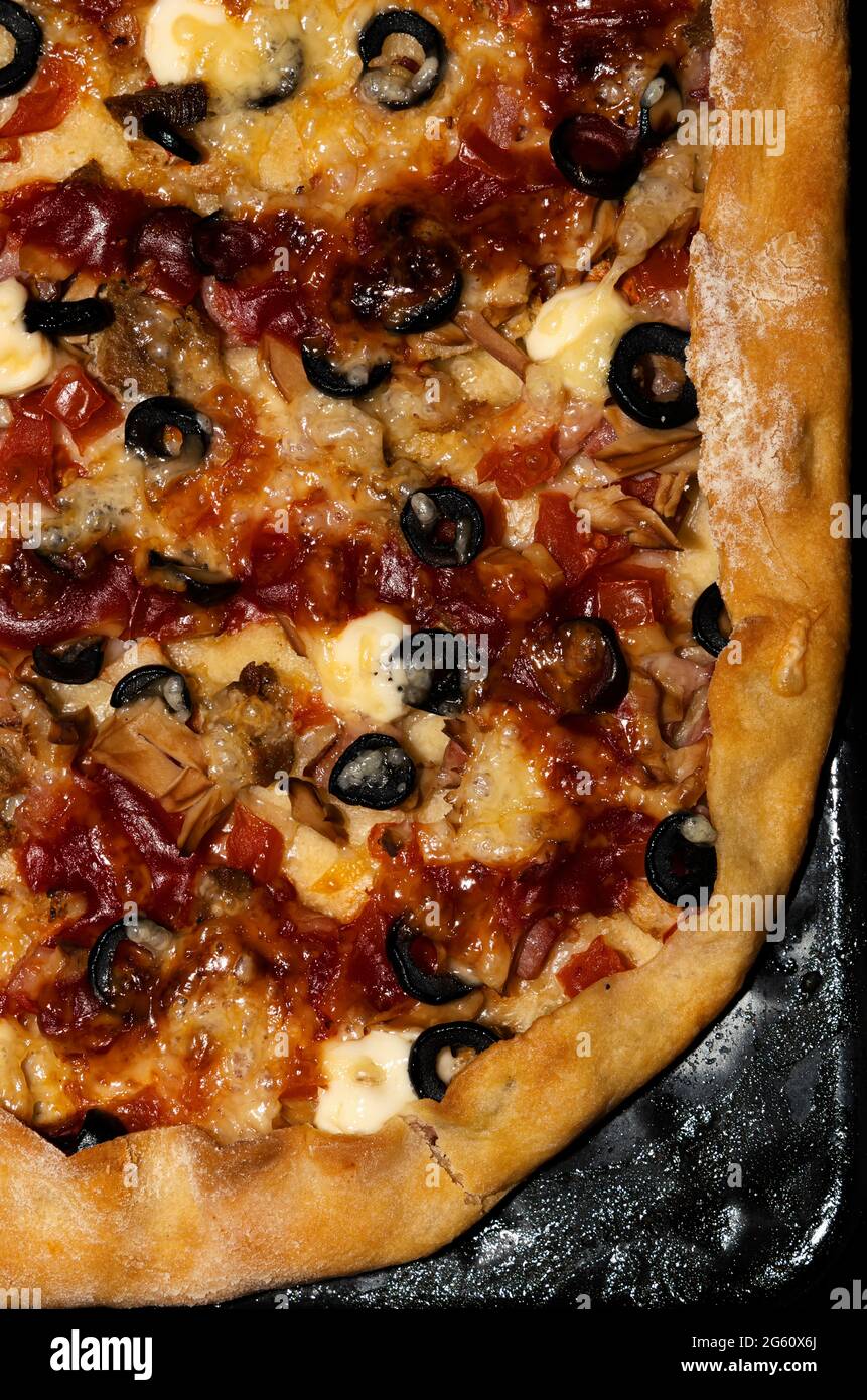 Tranche semi-circulaire de pizza avec olives, fromage, viande et tomates sur une plaque de cuisson à droite Banque D'Images