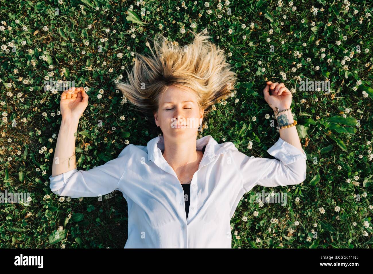 Vue de dessus d'une jeune femme allongé sur un pré avec un trèfle en fleur avec les yeux fermés. Banque D'Images