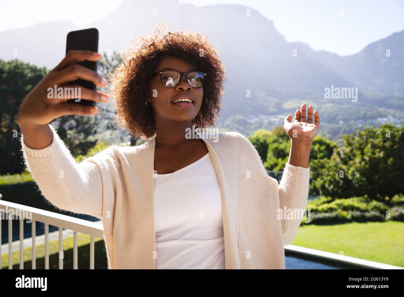 Bonne femme afro-américaine sur le balcon ensoleillé de la maison de campagne faire des appels vidéo sur smartphone Banque D'Images