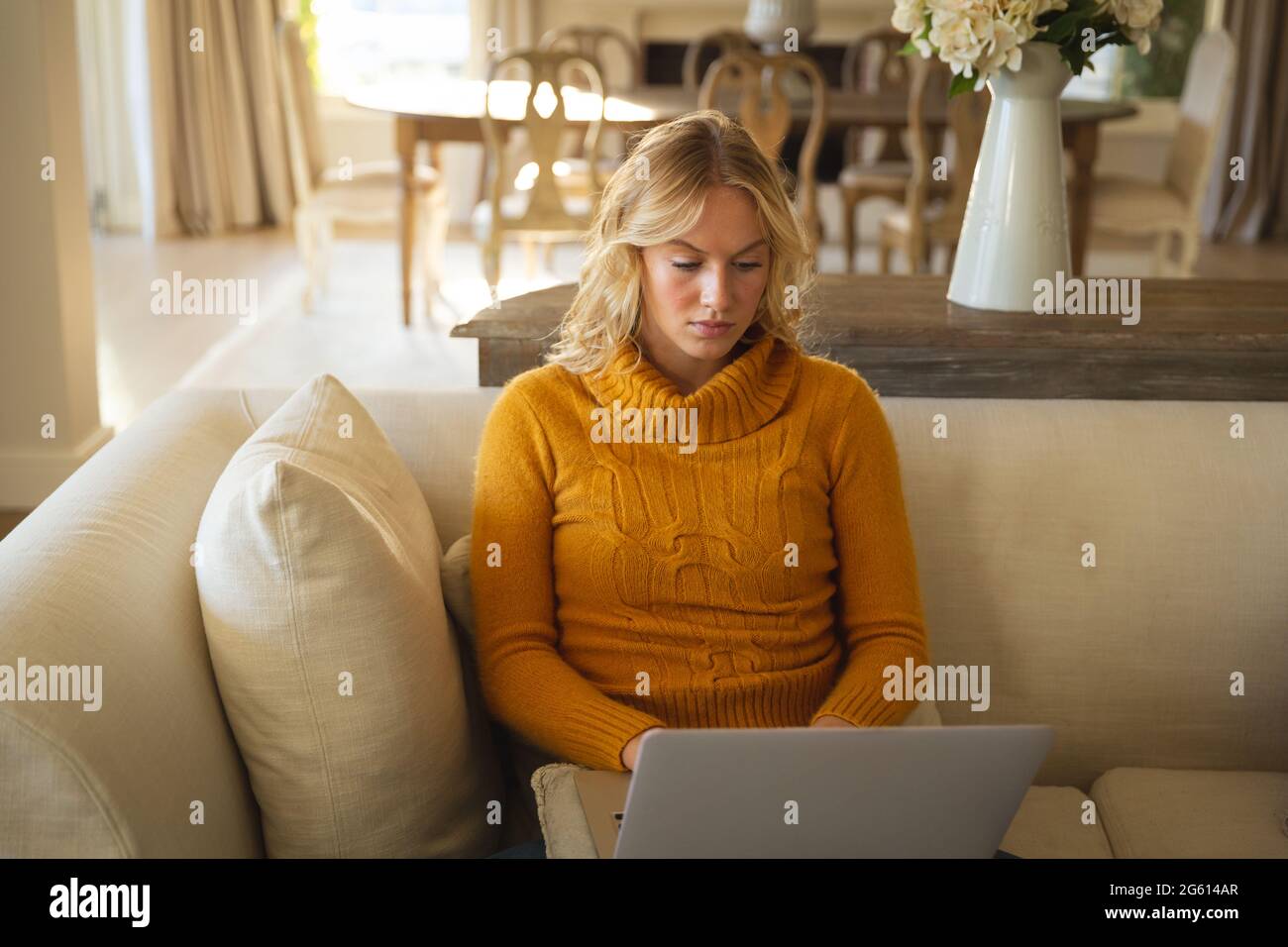 Femme caucasienne assise sur un canapé dans un salon de luxe utilisant un ordinateur portable, se concentrant Banque D'Images