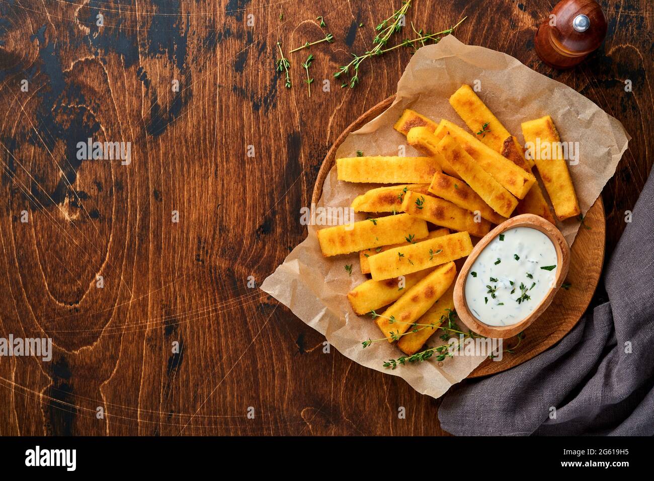 Croustilles de polenta faites maison frites avec sel de mer, parmesan, thym, romarin et sauce au yaourt. Polenta typiquement italienne. Bâtonnets de maïs frits. Dos en bois Banque D'Images