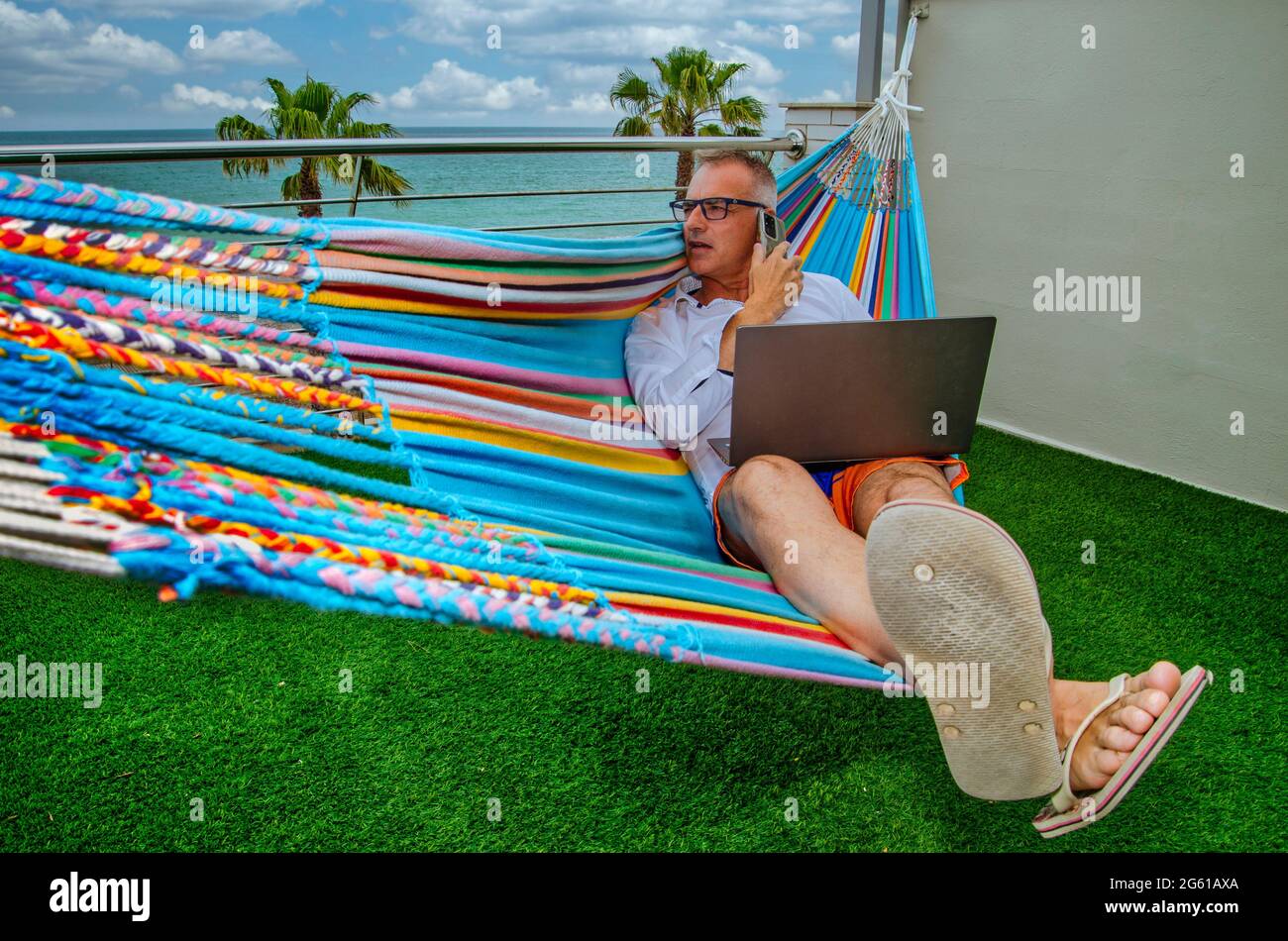 Homme d'affaires teleworking d'un endroit près de la mer dans un hamac Banque D'Images