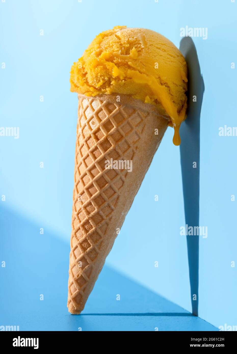 Crème glacée dans un cône de gaufres sur une table bleue en lumière vive. Pelle à glace Mango dans un cône, penchée sur un fond bleu. Banque D'Images