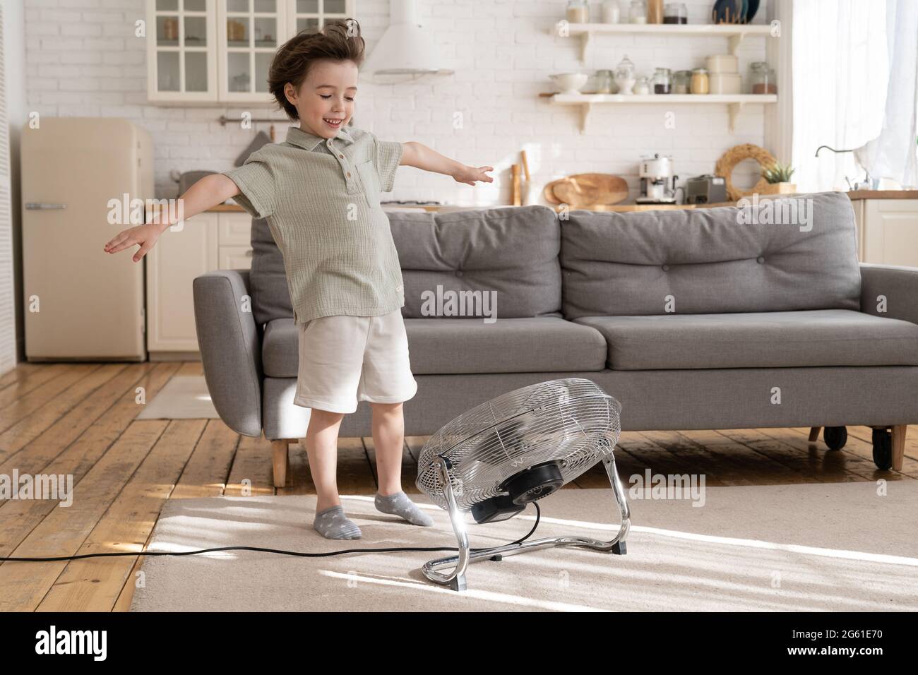 Joyeux gamin souriant, petit garçon d'âge préscolaire s'amuse avec ventilateur soufflant et flux d'air frais du ventilateur à la maison Banque D'Images