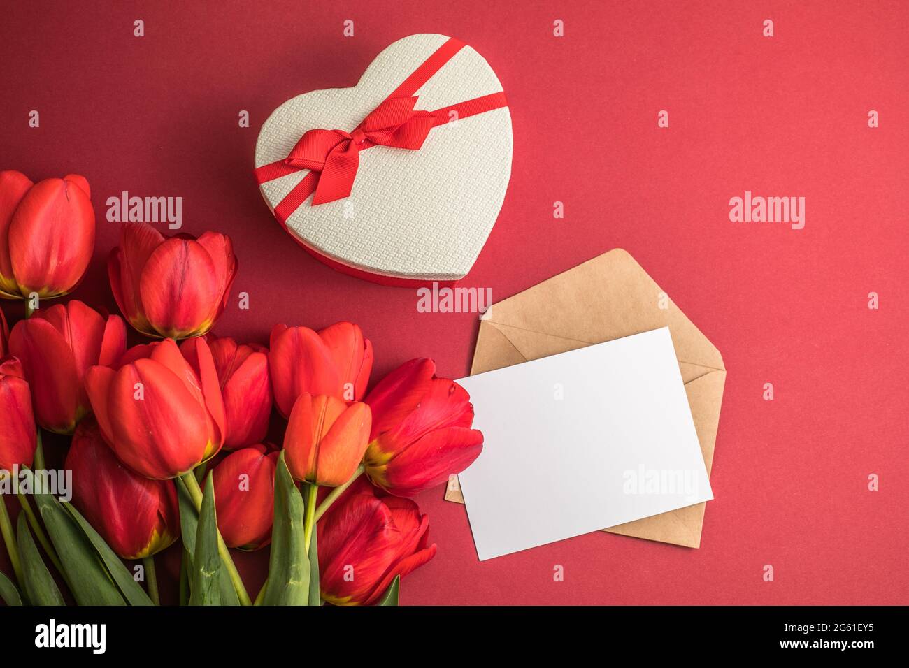 Bouquet de tulipes rouges et boîte cadeau de coeur isolée sur fond rouge . Fleurs de printemps. Carte de voeux pour anniversaire, femme, Fête des mères, mariage, Valen Banque D'Images