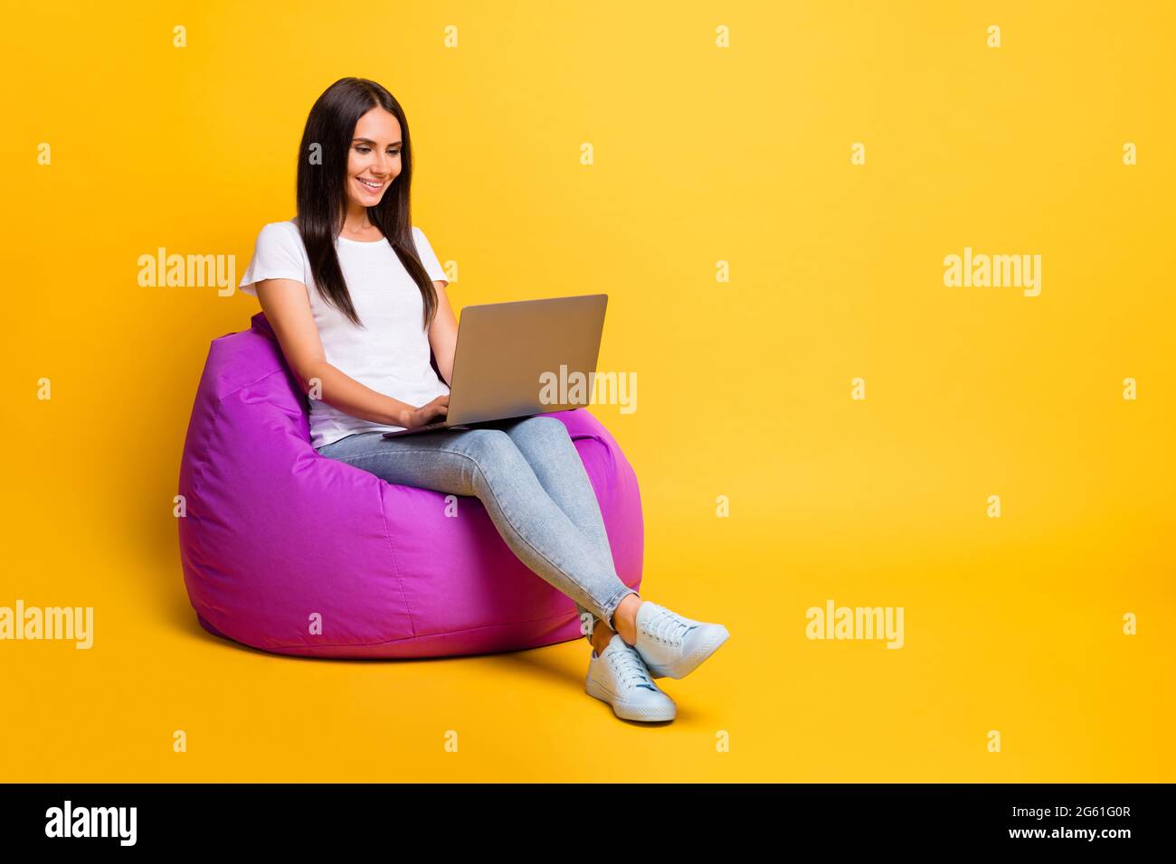 Pleine longueur de la photo de corps joli brunette travaillant avec la programmation d'ordinateur en violet beanbag isolé sur fond de couleur jaune vif Banque D'Images