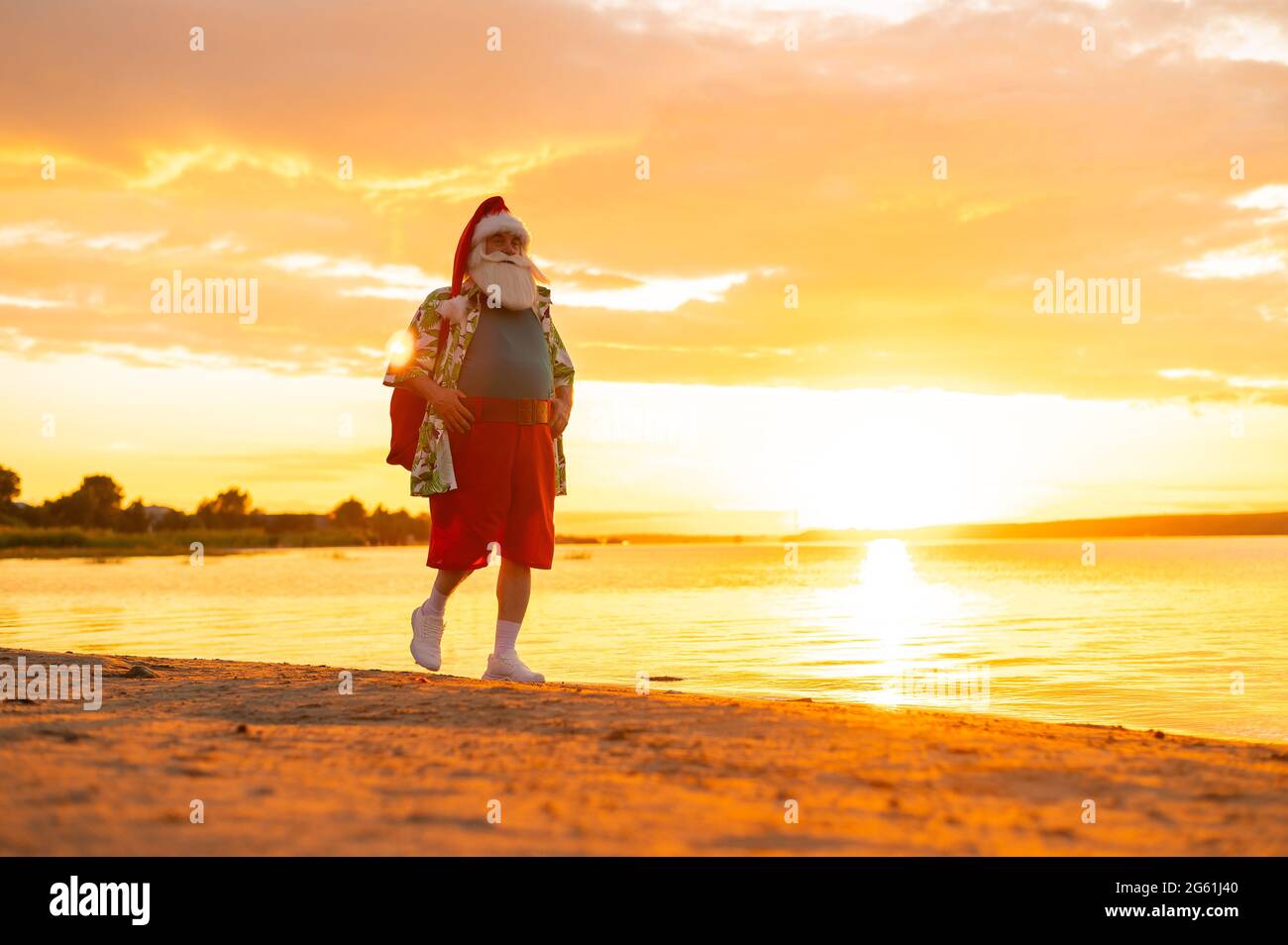 Le Père noël en short et une chemise marche le long de la plage au coucher  du soleil. Noël dans un pays chaud Photo Stock - Alamy