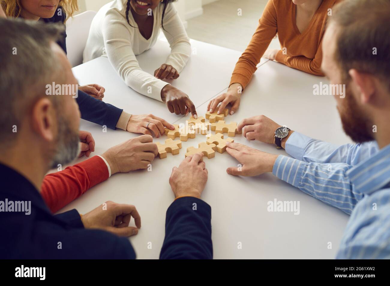 Une équipe variée de gens d'affaires assis autour d'une table et joignant des pièces de puzzle Banque D'Images