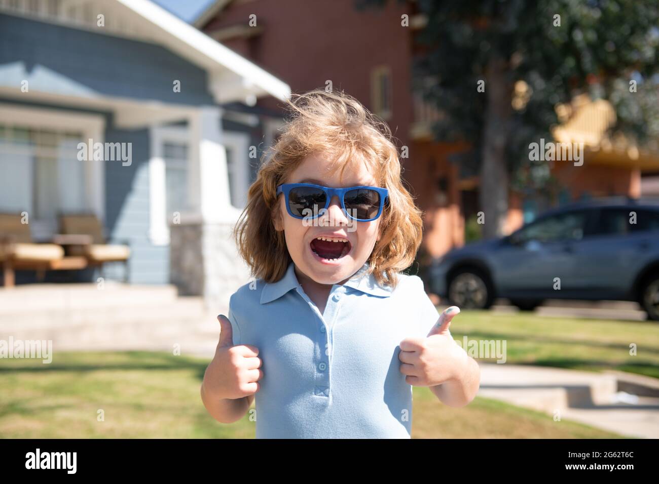 Portrait d'enfants excités dans des lunettes de soleil avec un signe de  pouce vers le haut, gros plan de la tête de l'enfant mignon à l'extérieur  de la maison, près de la