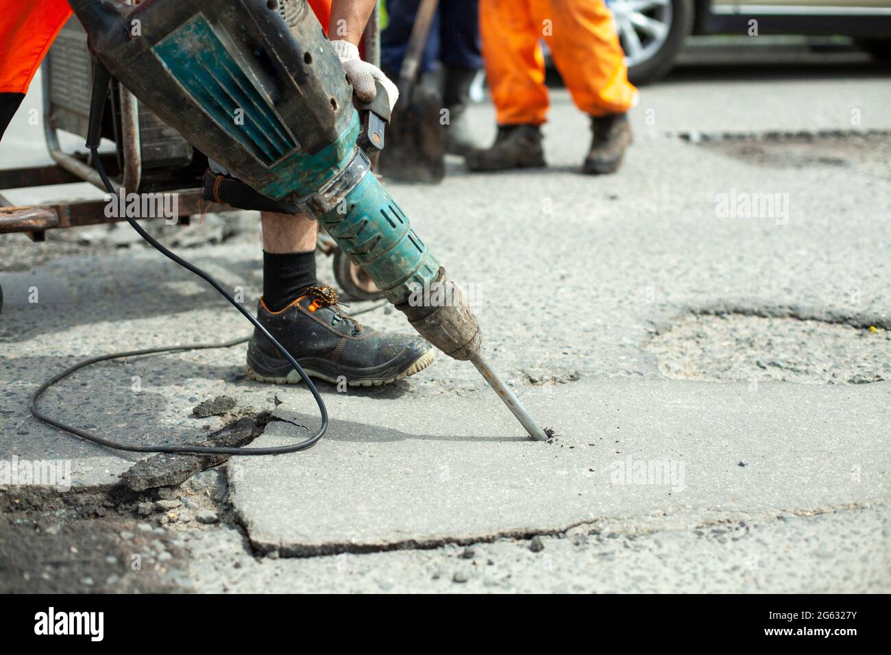 Il enlève l'asphalte avec un marteau à inertie. Retrait de la couche d'asphalte de la route. Le travailleur tient un marteau à inertie. Réparation sur route. Utilisation d'un hammam électrique Banque D'Images