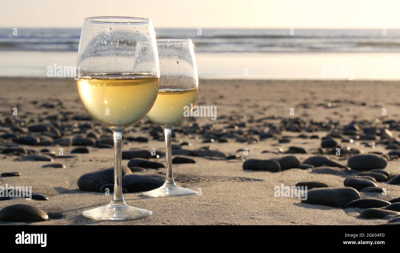 Deux verres de vin sur une plage de sable. Couple de verres et de cailloux,  vin blanc pour une date romantique près de l'eau de mer. Coucher de soleil  confortable sur la