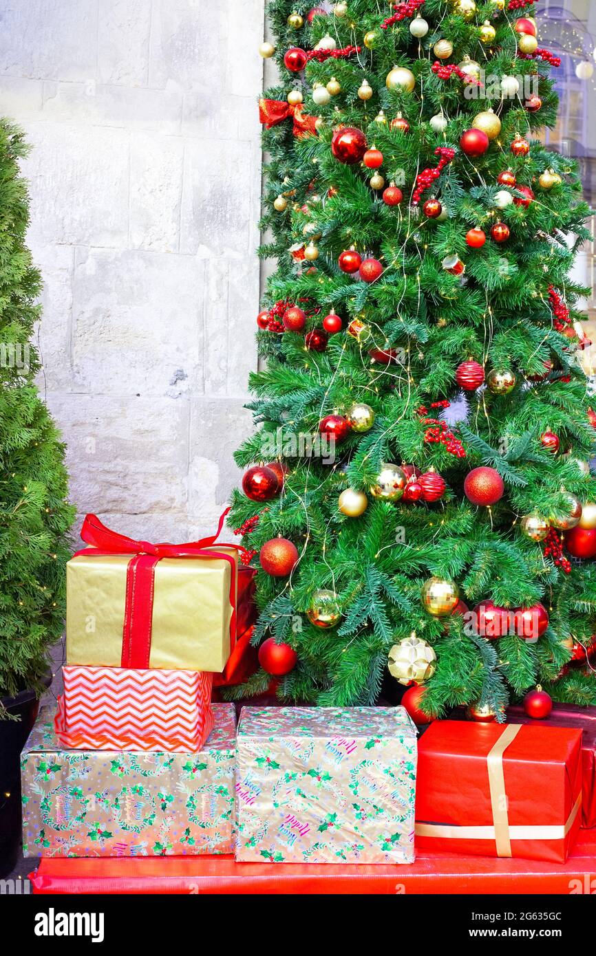Sapin de Noël décoré et boîtes cadeaux d'emballage près du mur de la maison. Décoration festive arbre vert et Santa présente dans l'emballage à la rue de ville Banque D'Images
