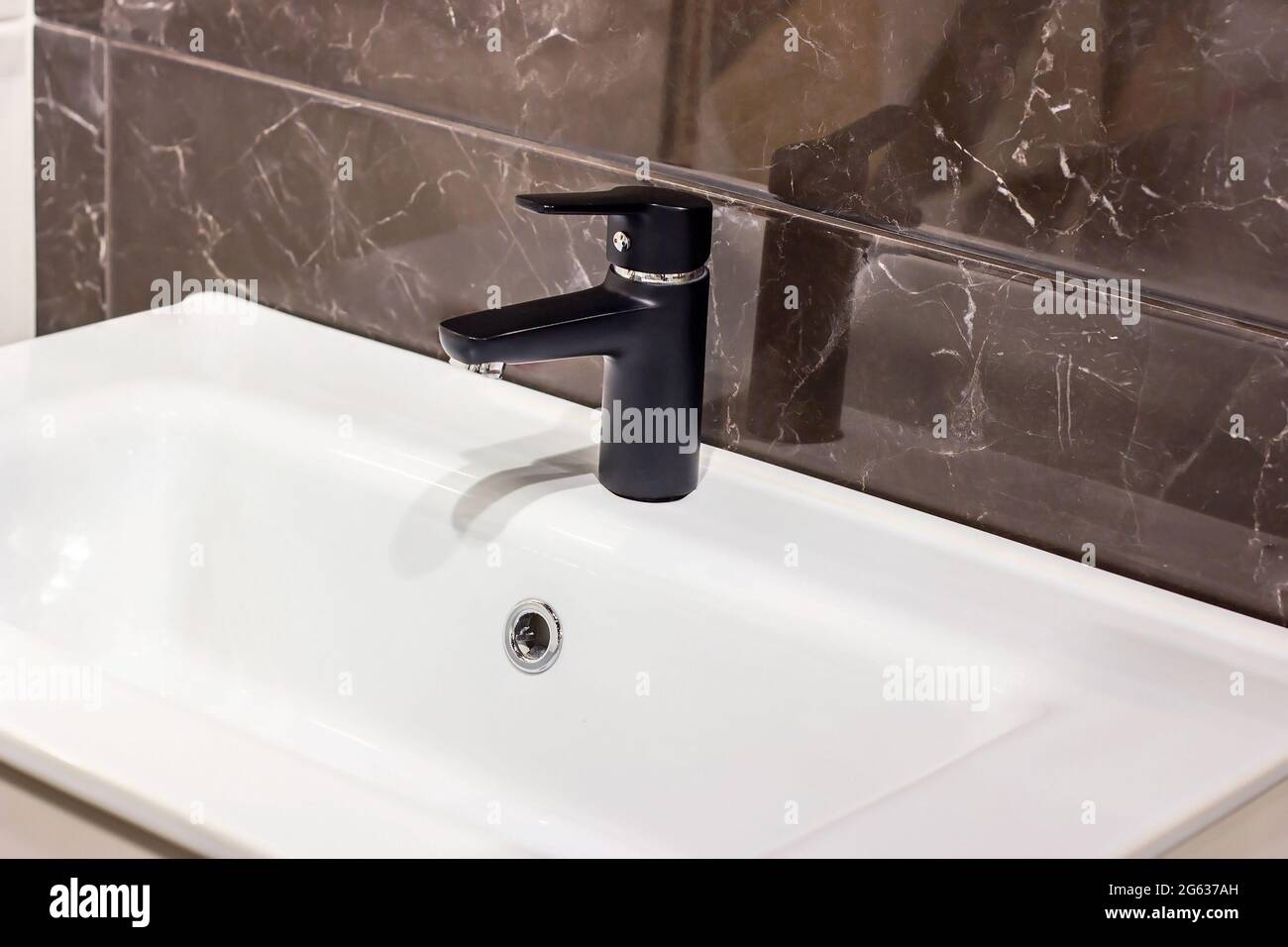 Nouveau robinet d'eau moderne noir avec le lavabo blanc sur le fond de mur en céramique dans la salle de bains. Banque D'Images