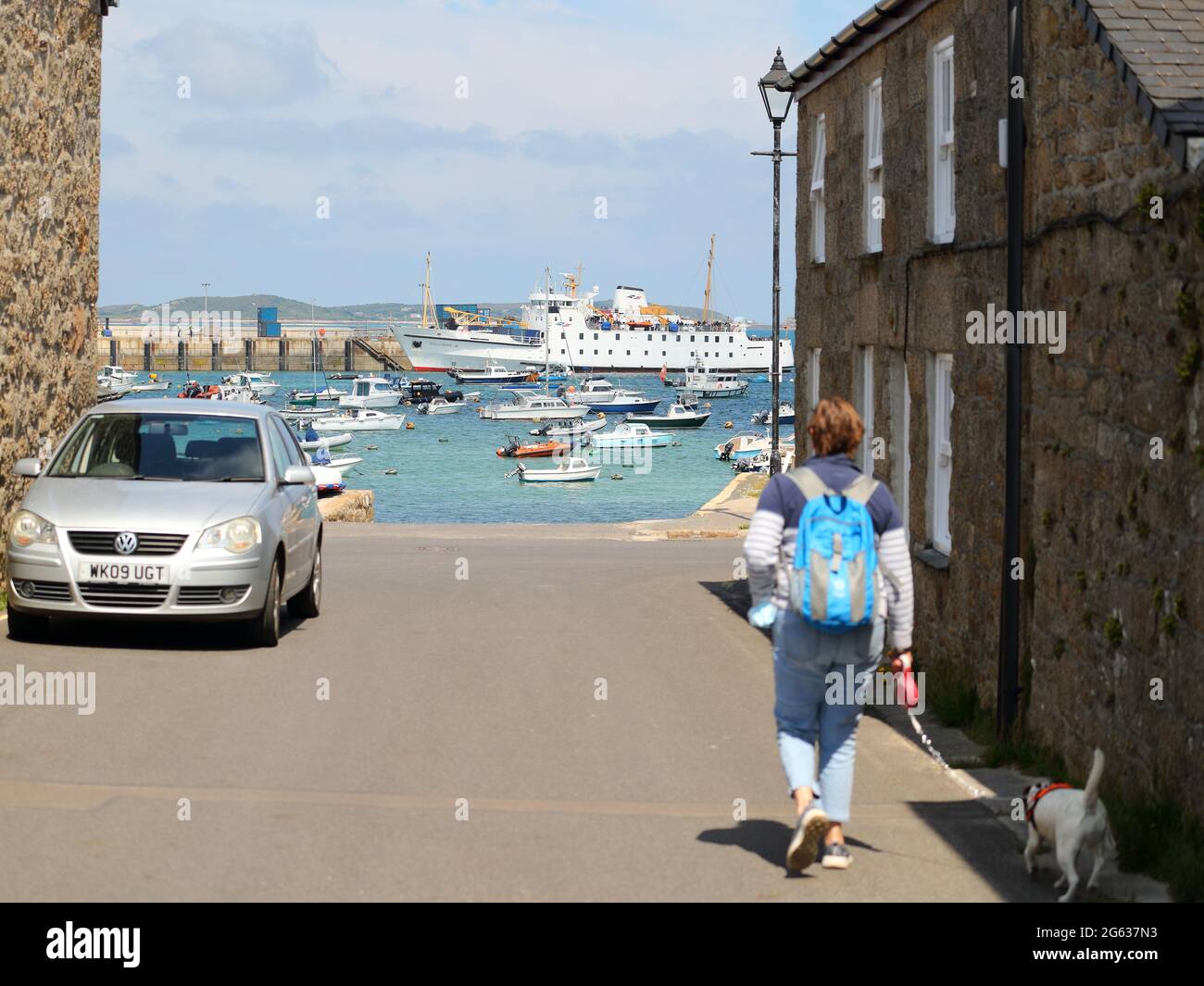 Une femme marche son chien vers le port de Hugh Town avec le Scillonian III amarré en arrière-plan, St Mary's, Isles of Scilly, Cornwall, Royaume-Uni Banque D'Images