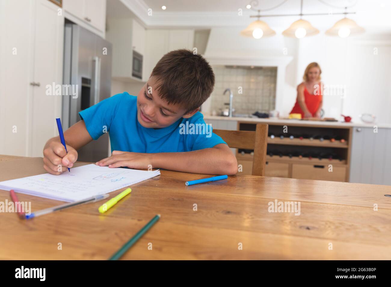 Mère caucasienne dans la cuisine et son fils faisant ses devoirs souriant à la maison Banque D'Images