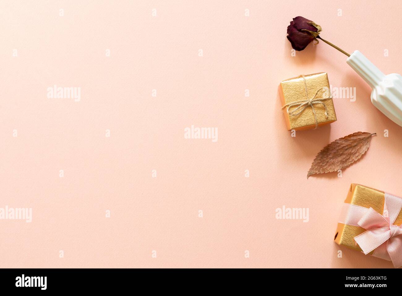 Boîtes-cadeaux dorées et fleur de rose sèche sur fond rose. Concept anniversaire. plan de travail, vue de dessus, espace copie Banque D'Images