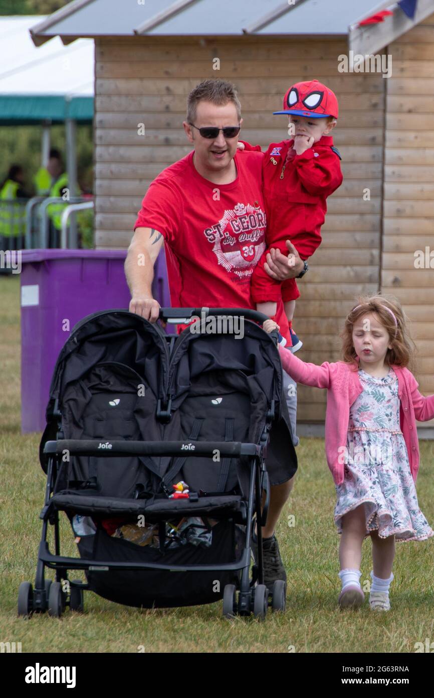 Un père ou un père poussant un buggy double en portant un enfant tandis que l'autre tient sur la poussette Banque D'Images