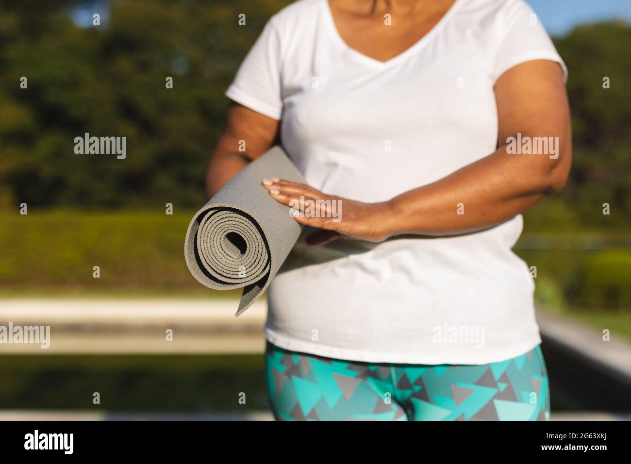 Section médiane de femme afro-américaine senior avec tapis de yoga près de la piscine extérieure dans la campagne Banque D'Images