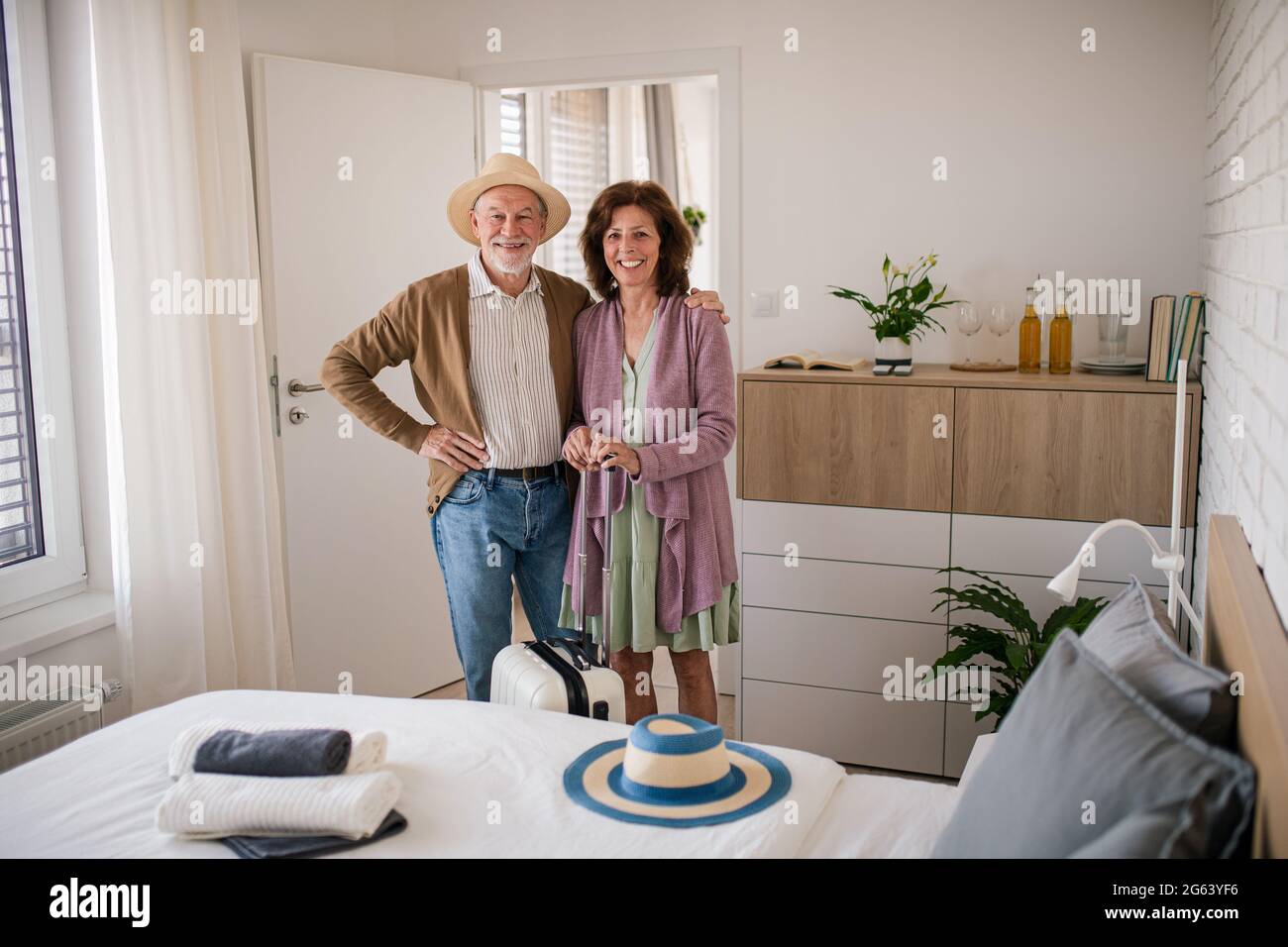 Couple senior heureux avec une valise dans la chambre d'hôtel, regardant la caméra. Banque D'Images