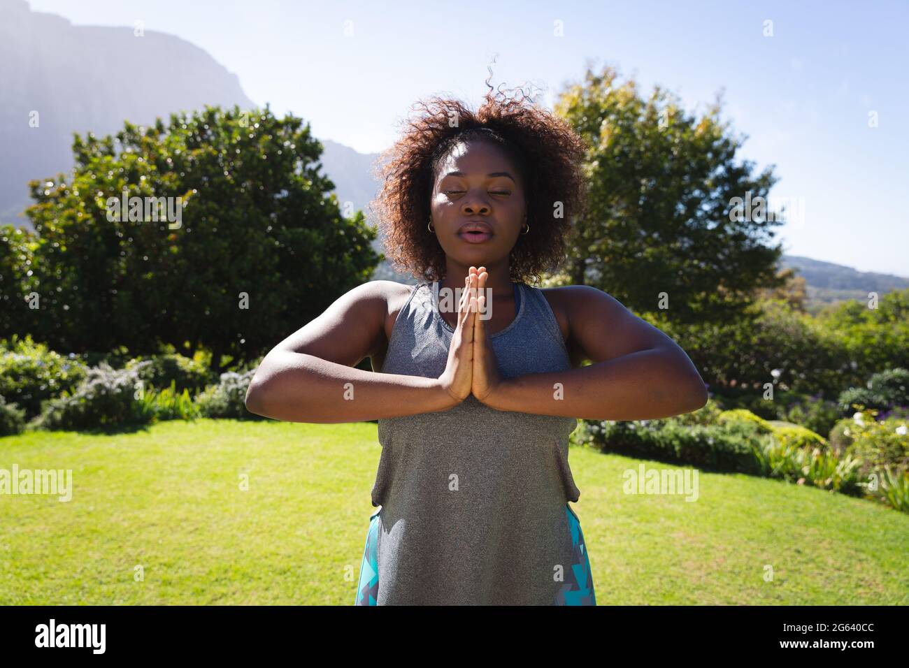 Section médiane de femme afro-américaine pratiquant le yoga avec les yeux fermés dans un jardin ensoleillé Banque D'Images