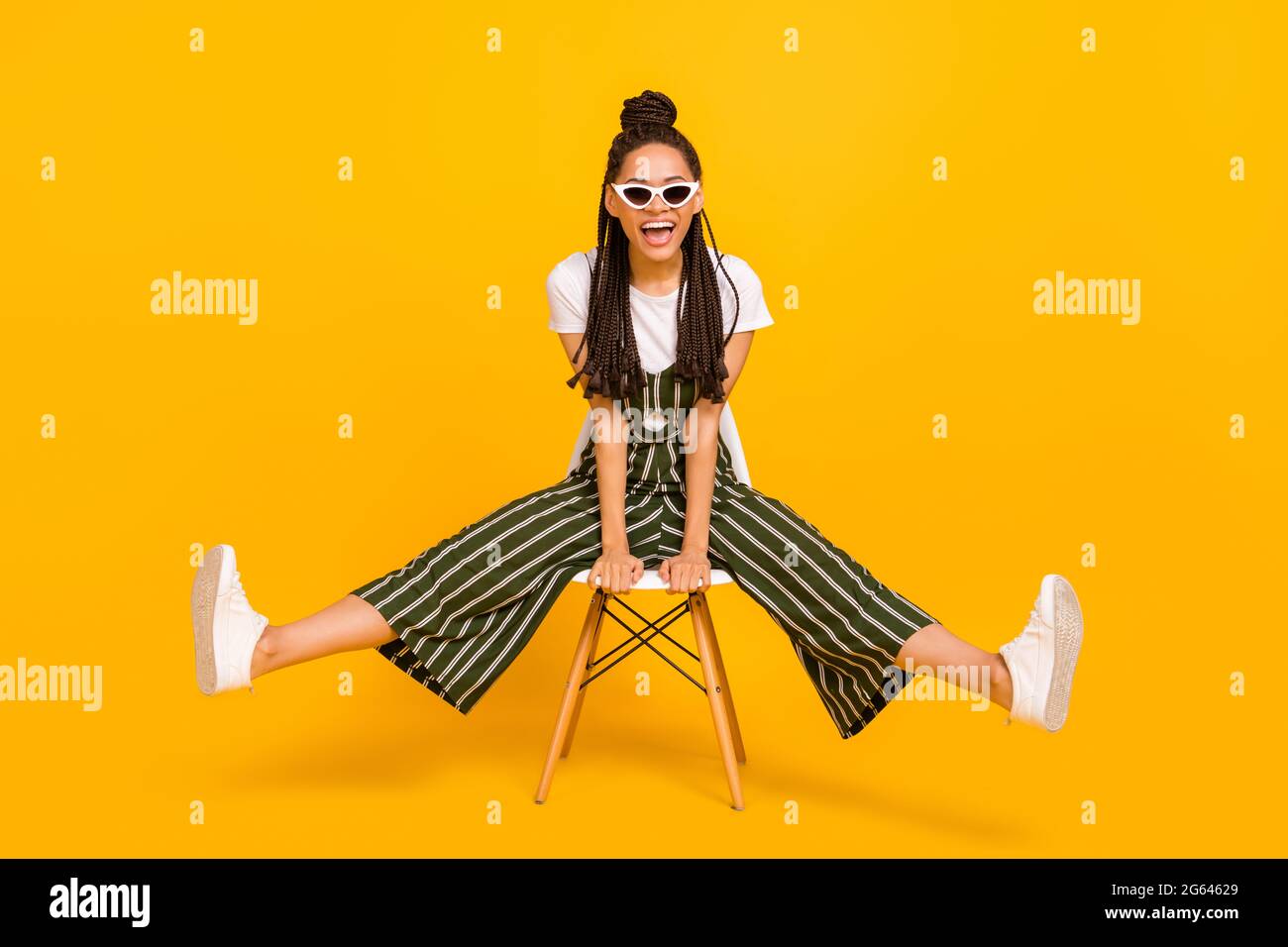 Photo du corps complet de la jeune fille africaine sourire heureux positif s'asseoir tabouret excité isolé sur fond jaune de couleur Banque D'Images