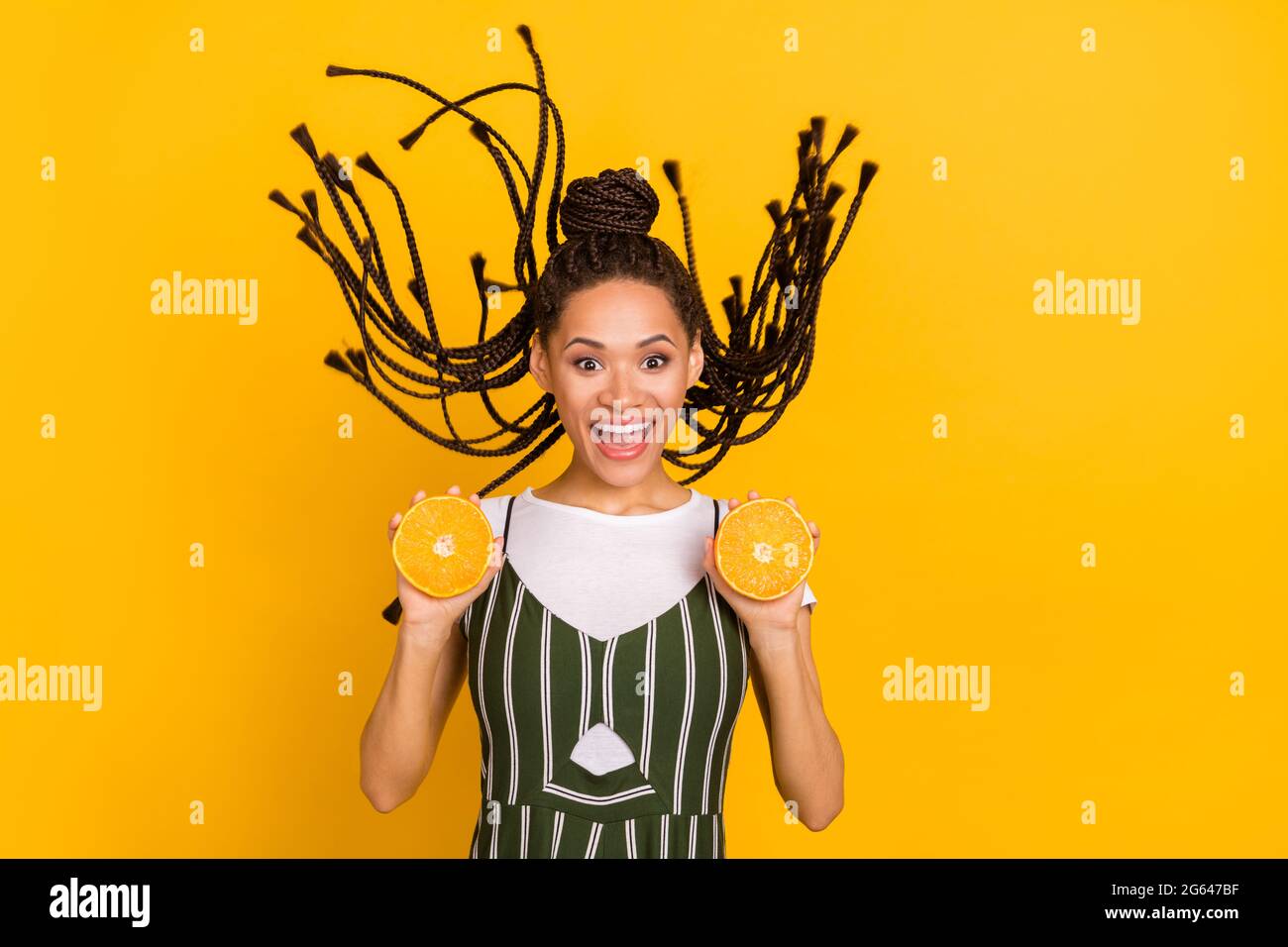 Photo de jeune afro-américaine gaie tenir des oranges mouche cheveux vent isolé sur fond jaune Banque D'Images