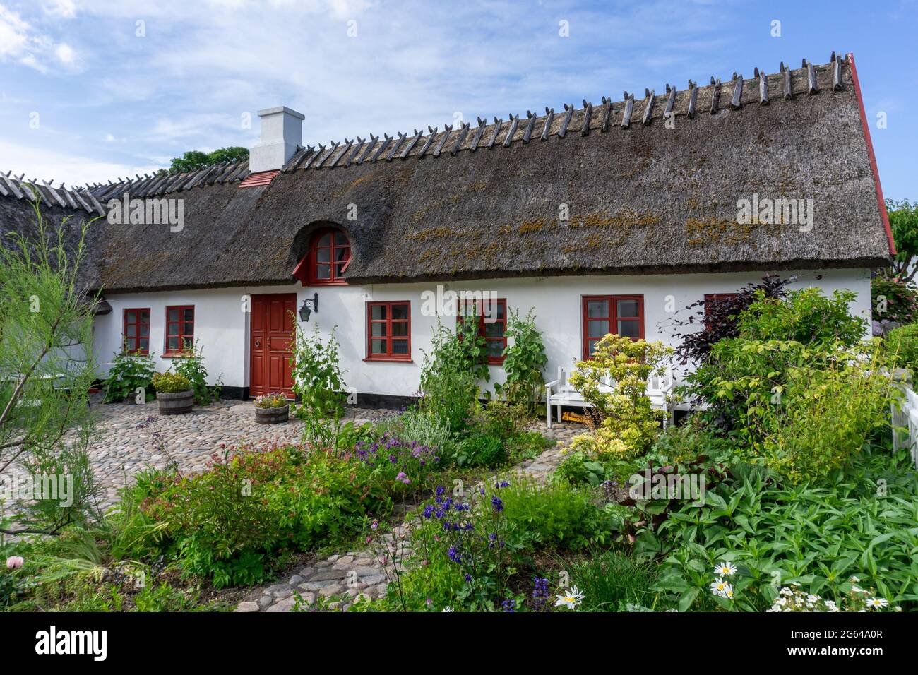 Gilleleje, Danemark - 15 juin, 2021: Belle maison en toit de chaume avec jardin potager sous un ciel bleu avec des cumulus blancs Banque D'Images