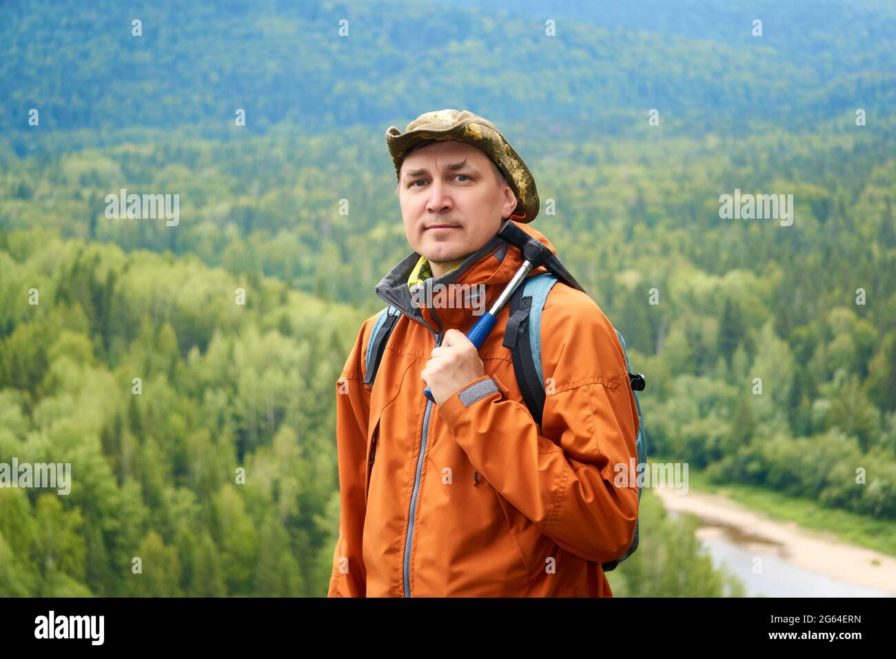 portrait d'un homme géologue avec un sac à dos et un marteau géologique en main contre le paysage de montagne boisée Banque D'Images