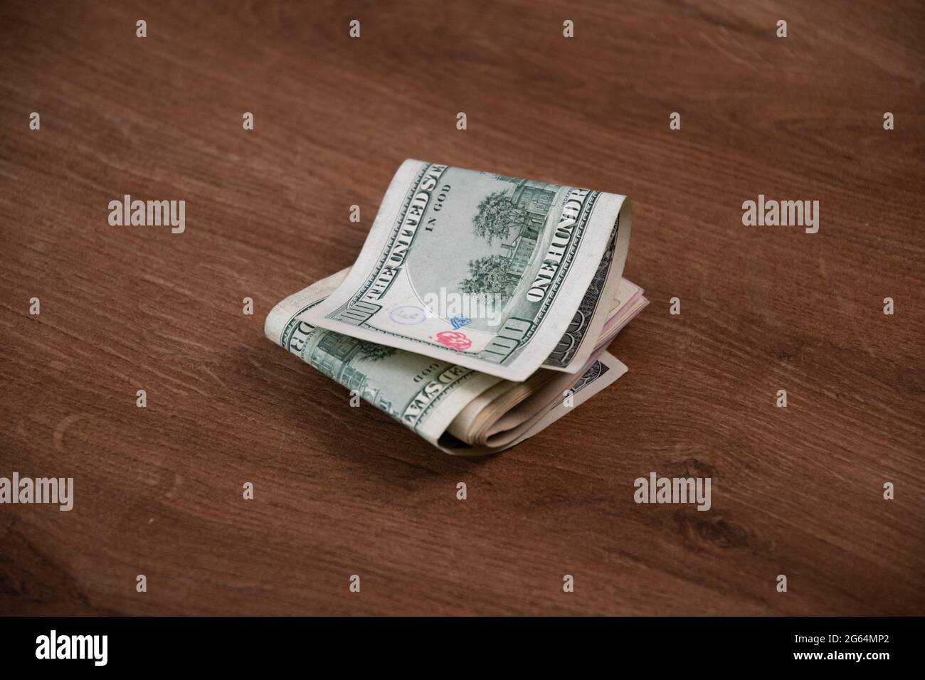 La pile d'argent des billets en dollars américains a été pliée en deux sur fond de bois. Un billet de cent dollars endommagé par des timbres d'encre Banque D'Images