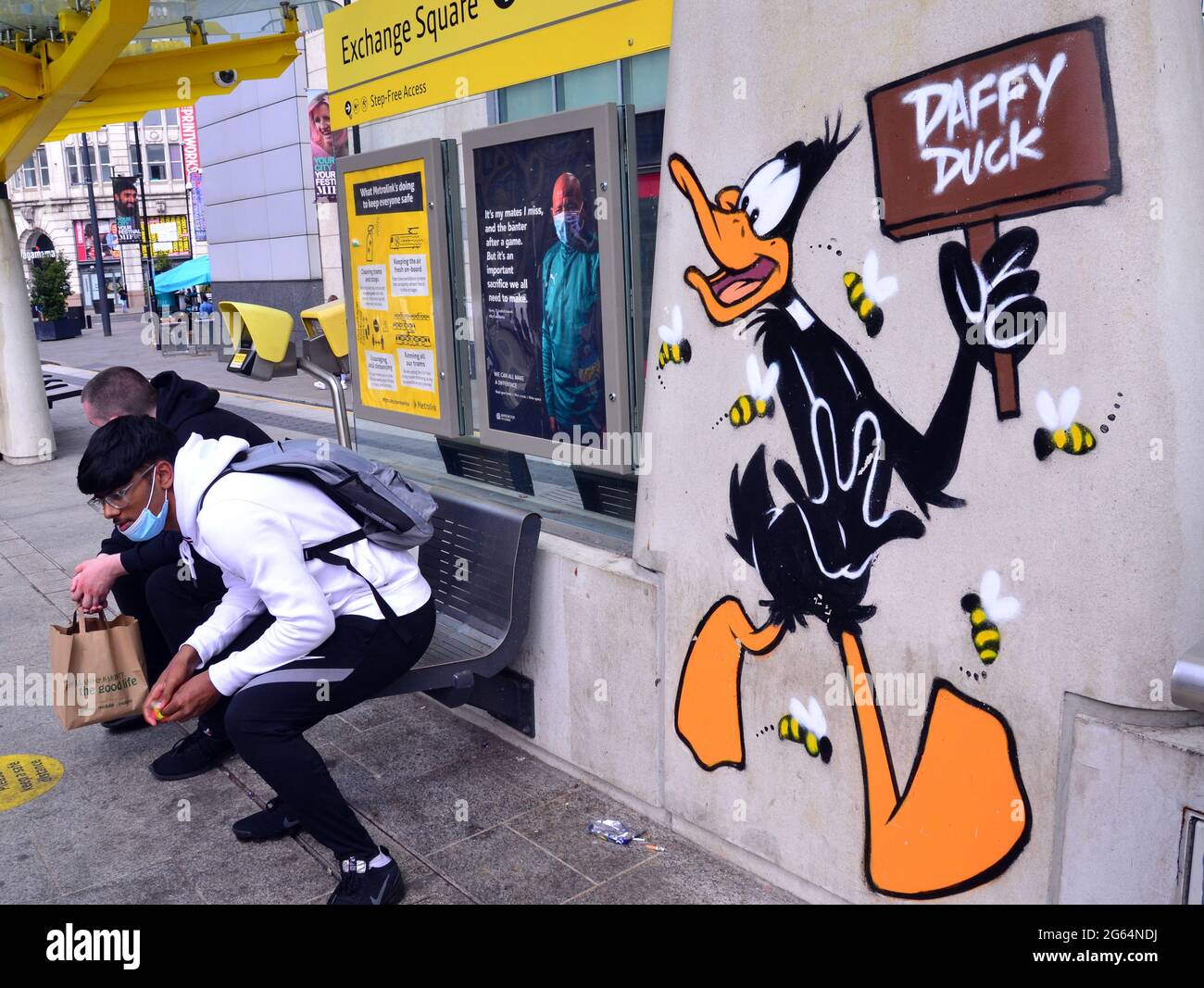Les hommes s'assoient à côté d'une image du personnage de dessin animé de Daffy Duck, qui fait partie d'un sentier d'art de Looney Tunes qui a ouvert ses portes à Manchester, en Angleterre. Banque D'Images