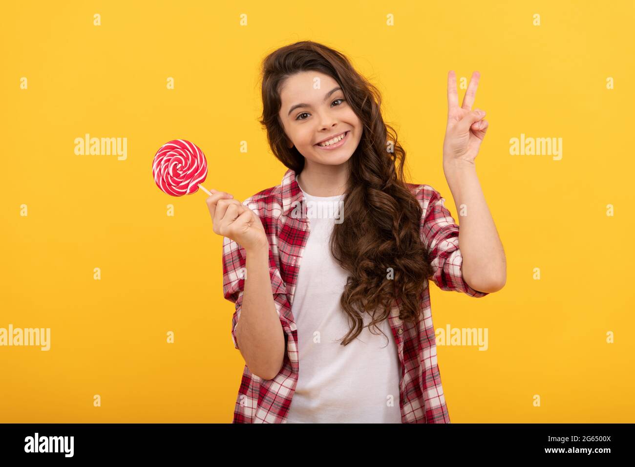 drôle enfant tenir lollipop caramel bonbon sur fond jaune montrer le geste de paix, l'enfance. Banque D'Images