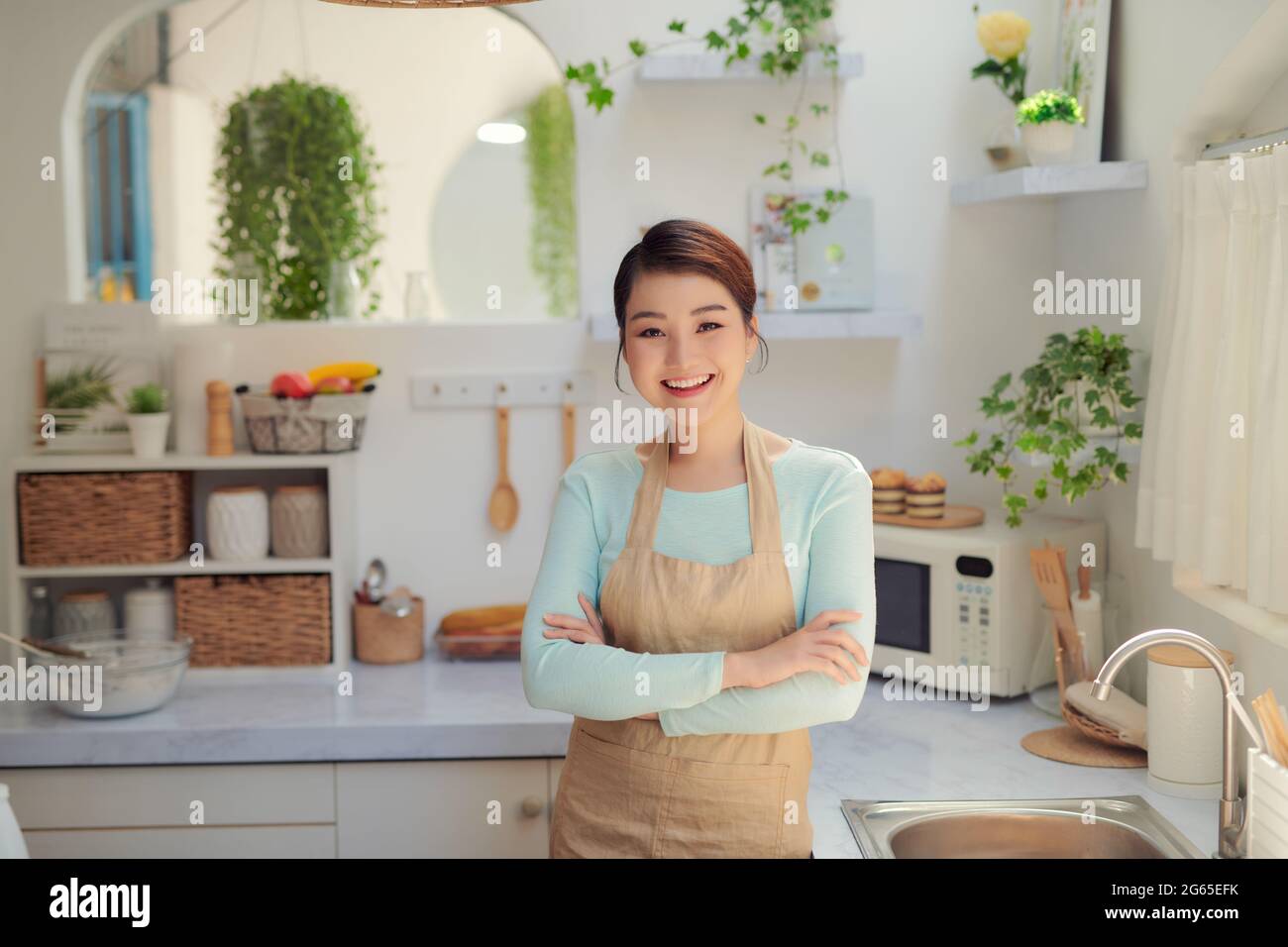 Portrait asiatique jeune heureux belle femme souriante debout croisant les mains sur la cuisine Banque D'Images