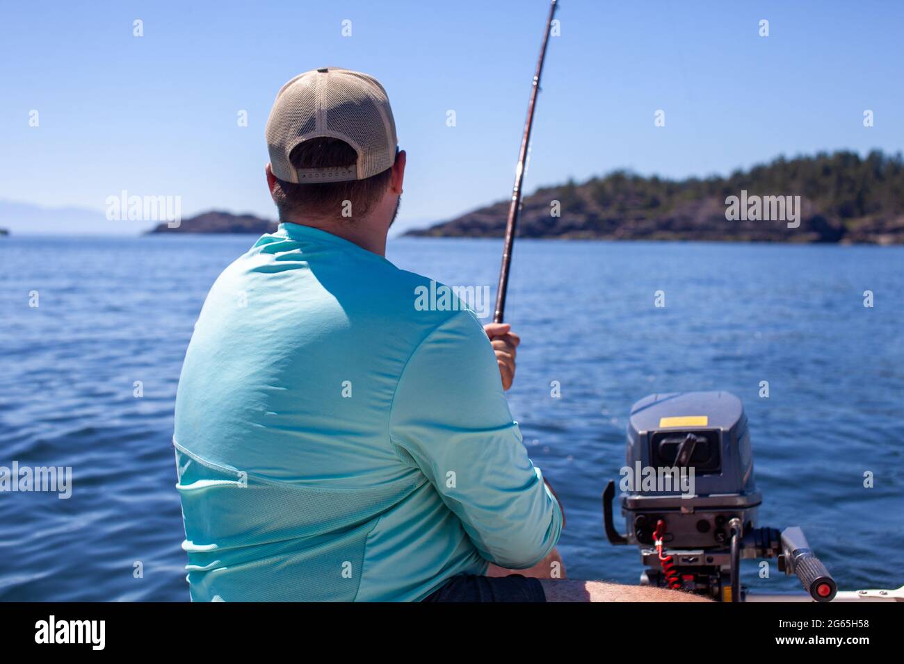Un homme tient une canne à pêche, en trolling pour le saumon le long de la côte de la Colombie-Britannique, dans un petit canot pneumatique de zodiaque portant une chemise de soleil et un chapeau Banque D'Images