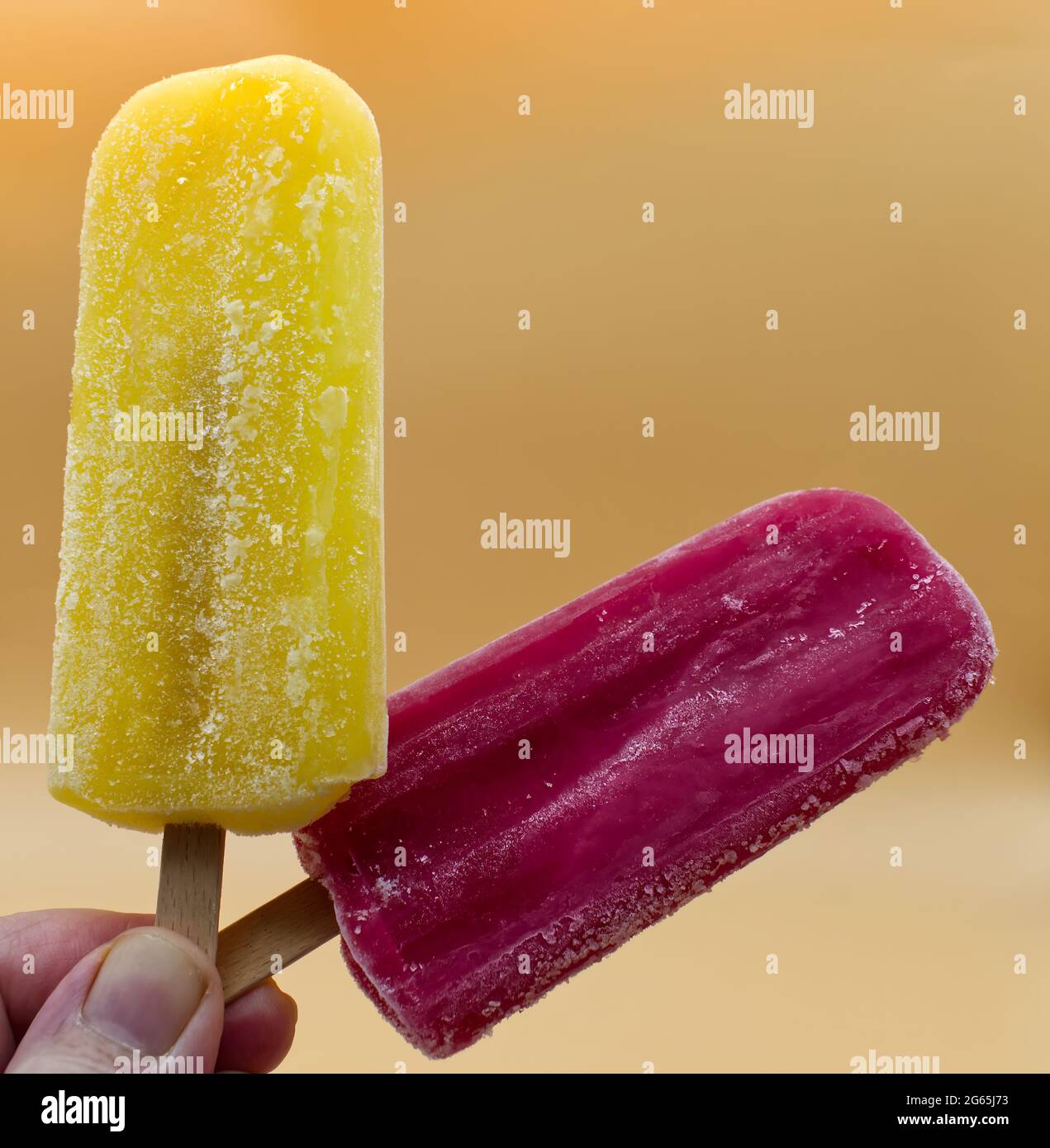 Main tenant la Popsicle jaune et violet sur un fond jaune Banque D'Images
