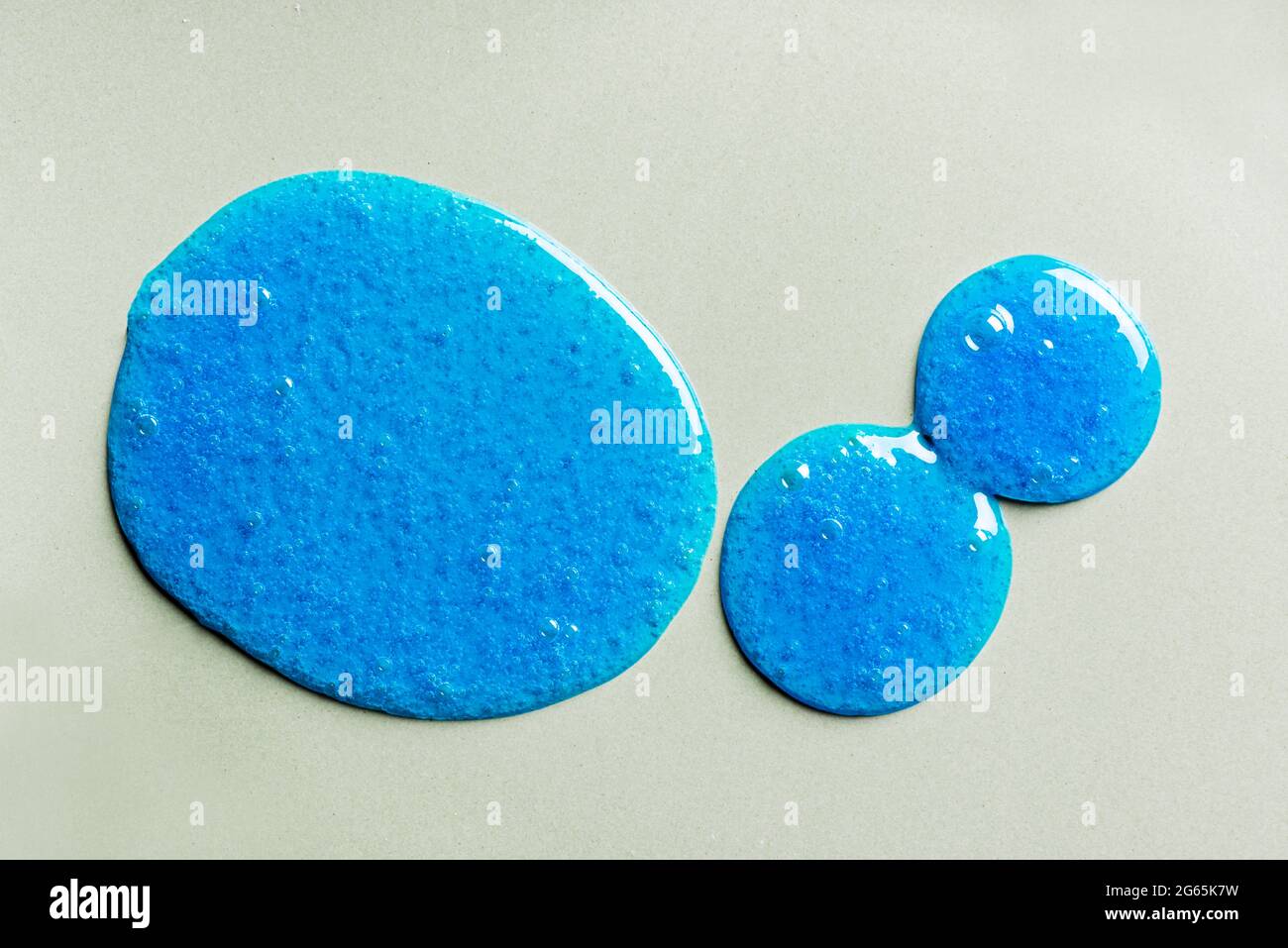 L'échantillon de shampooing bleu ou de gel douche tombe sur fond gris. Produit cosmétique Blue Gel avec bulles. Banque D'Images