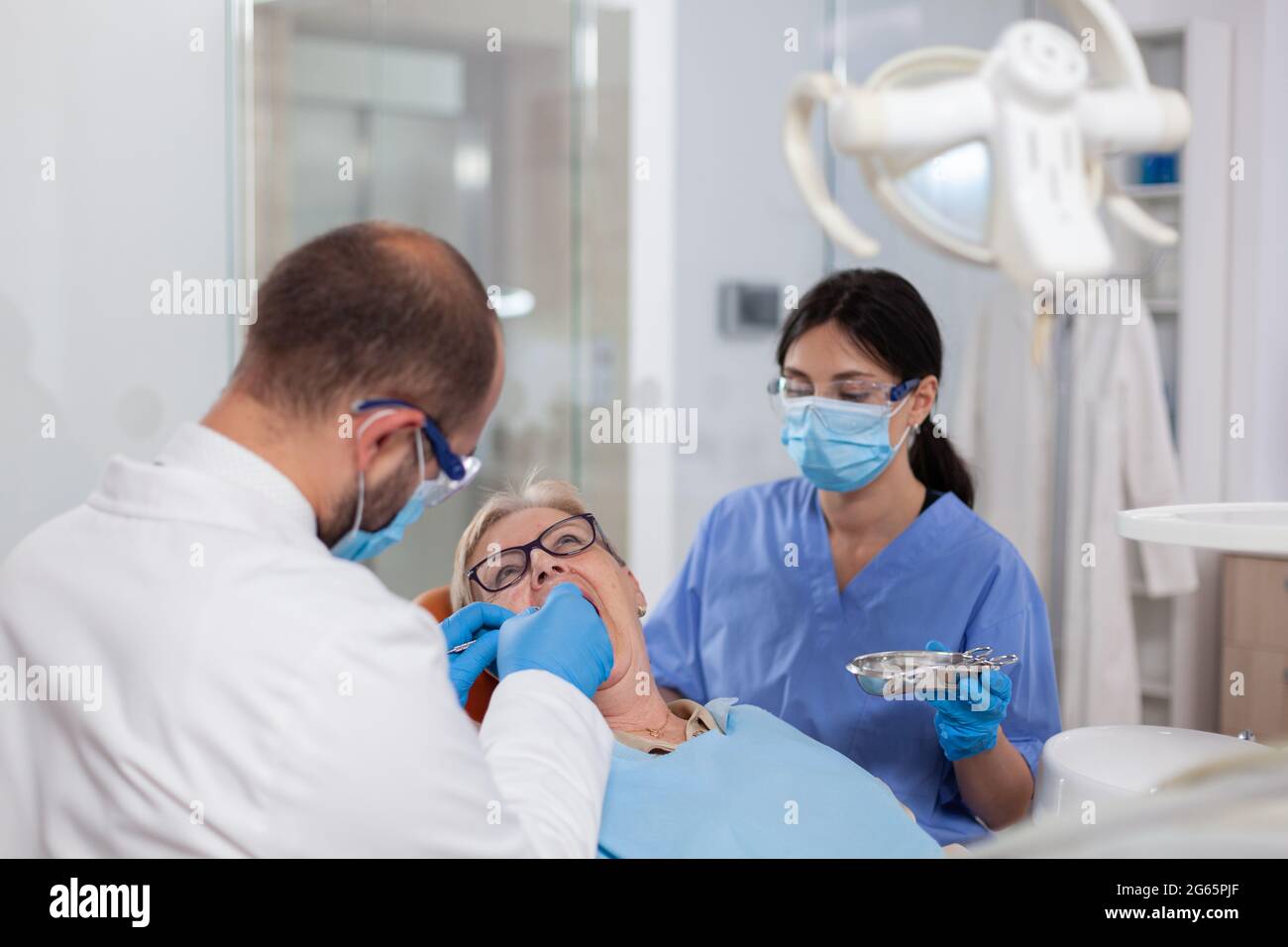 Stomatolog avec assistant de pose de joint dentaire sur les dents de femme âgée. Patient âgé pendant un examen médical avec un dentiste dans un cabinet dentaire équipé d'un équipement orange. Banque D'Images