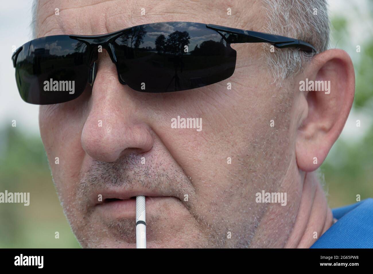 visage d'un homme en lunettes de soleil sombres gros plan avec une cigarette, arrière-plan flou avec des éléments bokeh. Photos. Banque D'Images