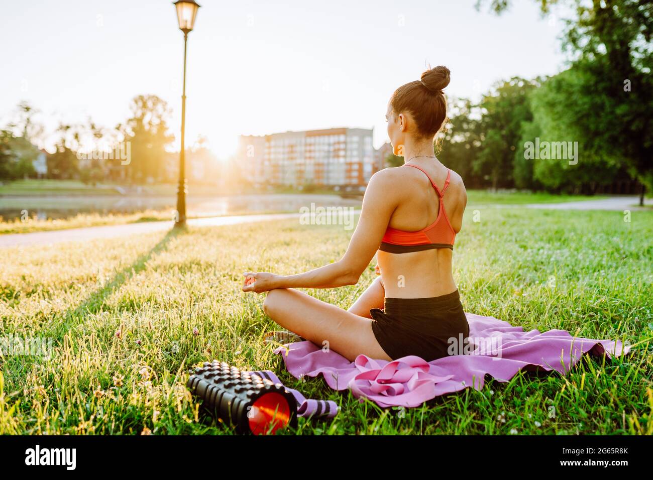 Femme portant des vêtements de sport pratiquant le yoga dans le parc. Une femme s'assoit en position lotus et médite au lever du soleil. Banque D'Images