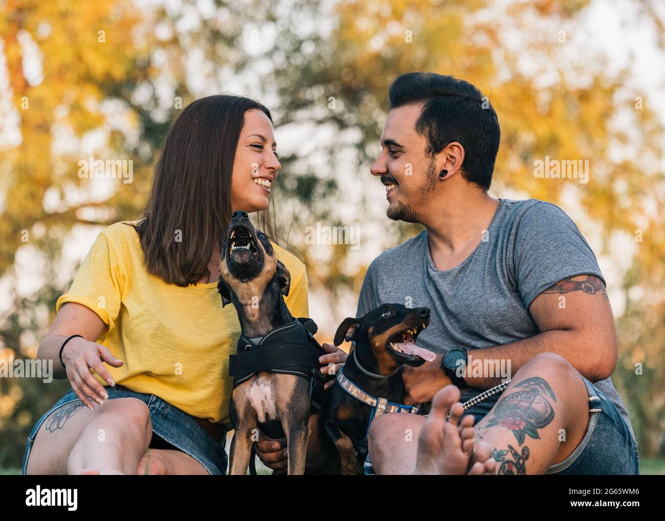 Jeune couple heureux se regardant les uns les autres avec leurs chiens dans un parc Banque D'Images