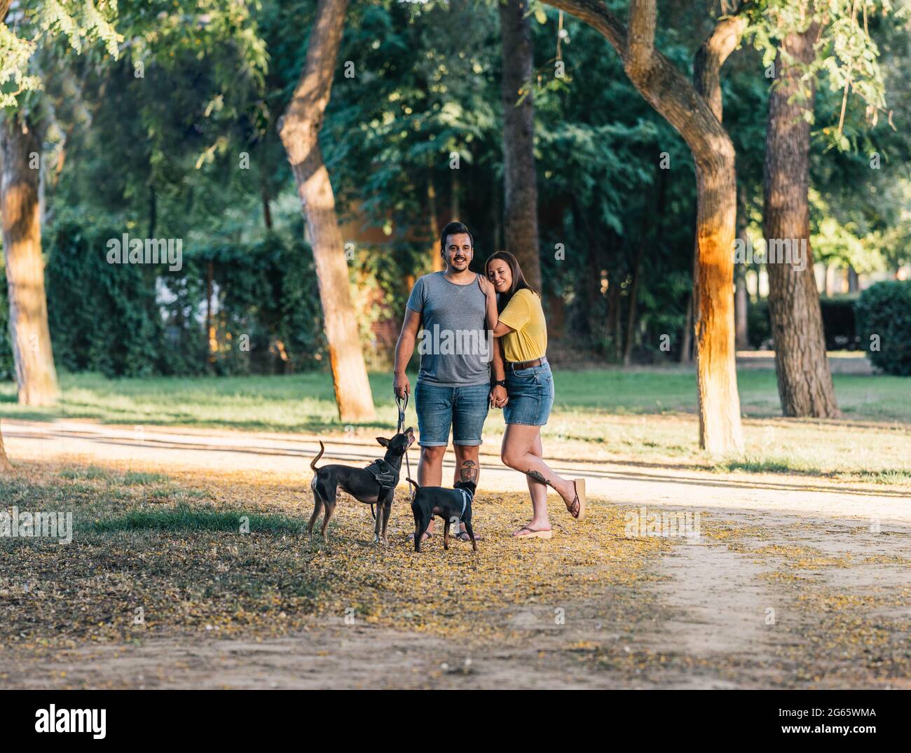 Couple posant avec leurs deux chiens dans un parc Banque D'Images