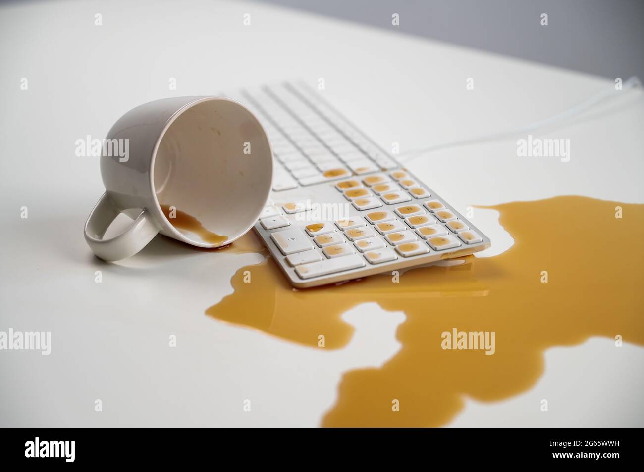 Tasse de café noir renversée sur le clavier de l'ordinateur sur la table blanche. Banque D'Images Tasse de café noir renversée sur le clavier de l'ordinateur sur la table blanche. Banque D'Images
