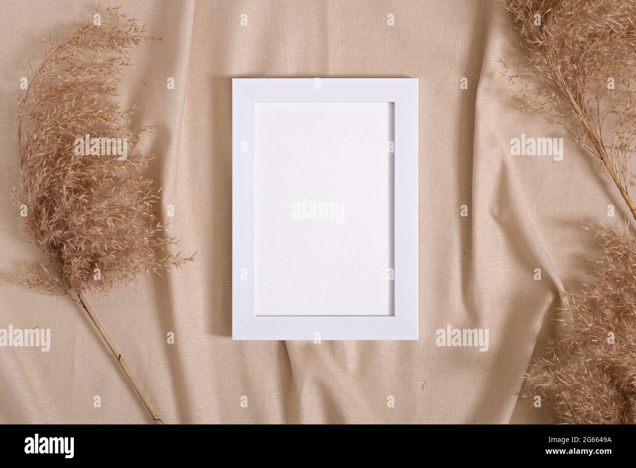 Cadre photo avec maquette de carte papier vierge à proximité des pampas herbe sèche sur tissu beige de couleur neutre Banque D'Images