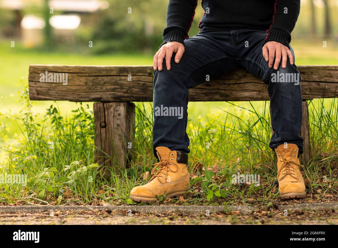 Homme ouvrier ou fermier portant des vêtements et des chaussures  décontractés assis, se reposant et relaxant, appréciant la nature dehors  sur un banc rustique à côté d'une gra verte Photo Stock -