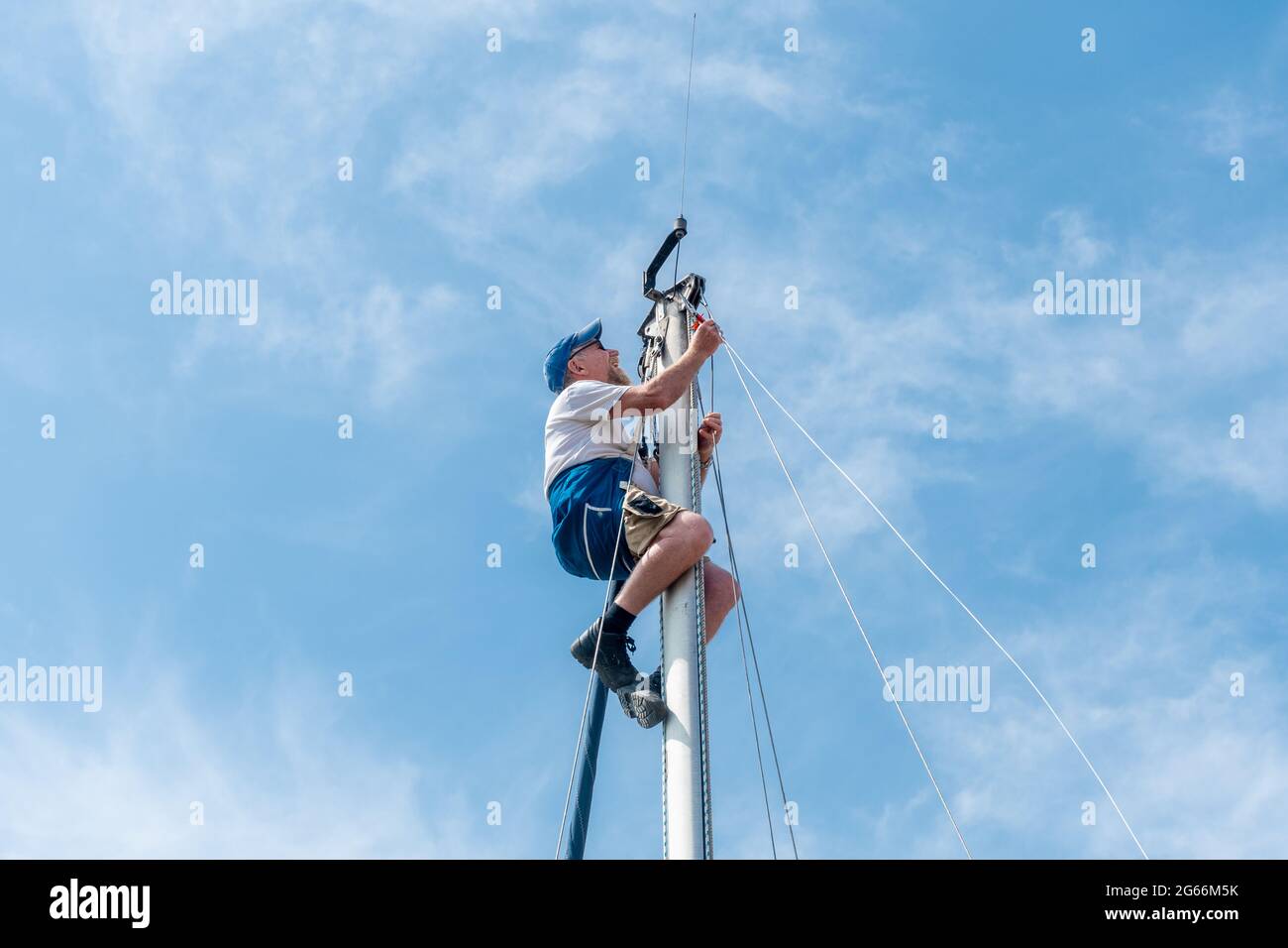 Homme dans un harnais de sécurité en haut du mât d'un yacht ou d'un voilier effectuant des travaux d'entretien sur le gréage, Royaume-Uni Banque D'Images