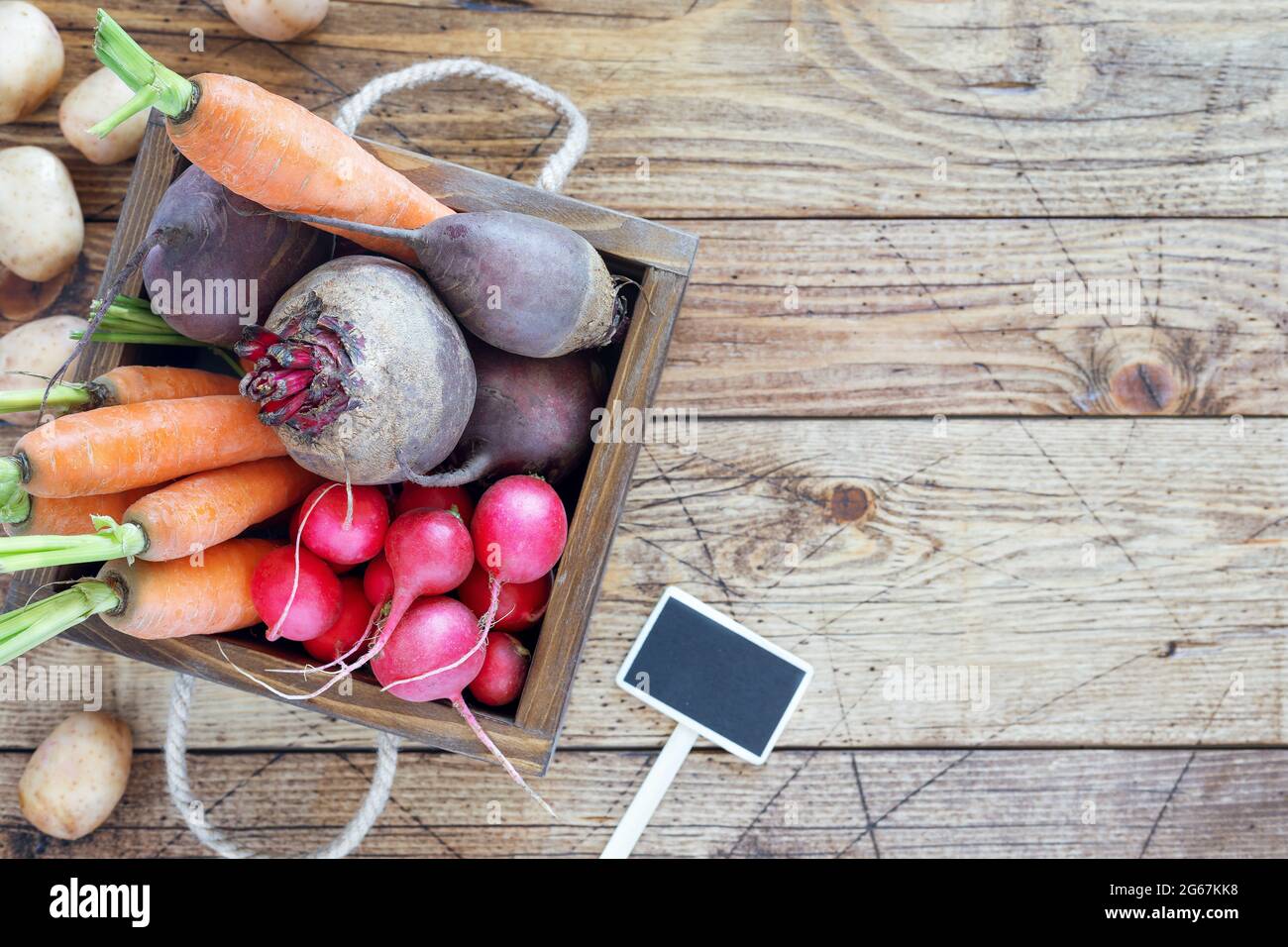 Bio, légumes de ferme : carottes, betteraves, radis, pommes de terre et ail dans une boîte en bois sur fond de bois. Vendre des légumes de saison Banque D'Images