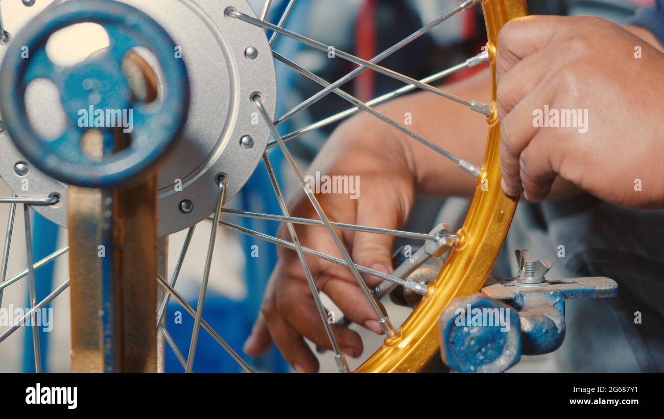 Le technicien qui travaille la roue de moto a des rayons qui serpentent sur  une nouvelle roue en acier mécanique, des rayons de moto outil de  parallélisme de roue Photo Stock -