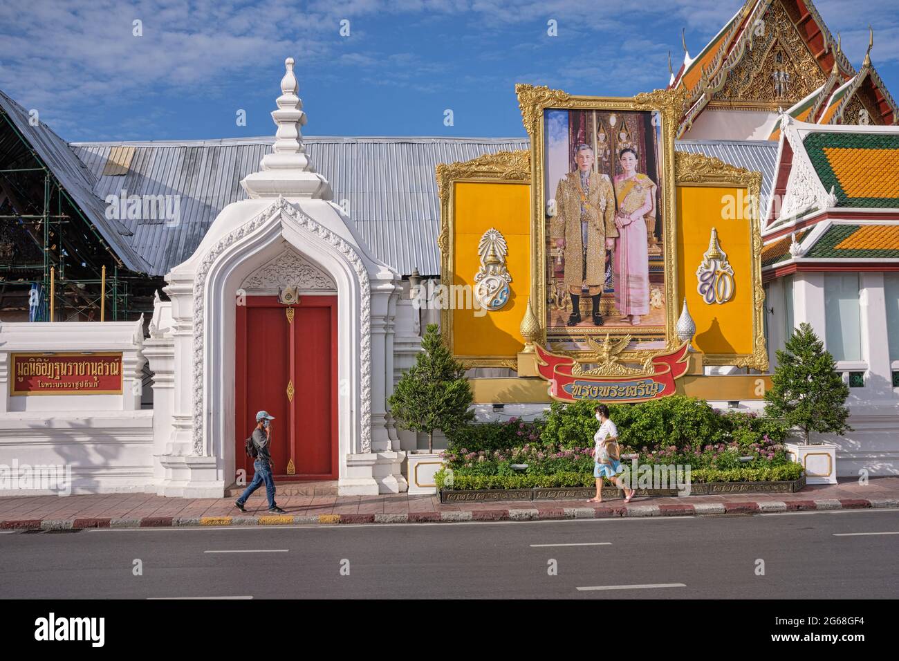 Piétons passant sous un grand portrait du roi Maha Vajiralongkorn et de la reine Suthida de Thaïlande, érigée à (temple) Wat Suthat, Bangkok, Thaïlande Banque D'Images