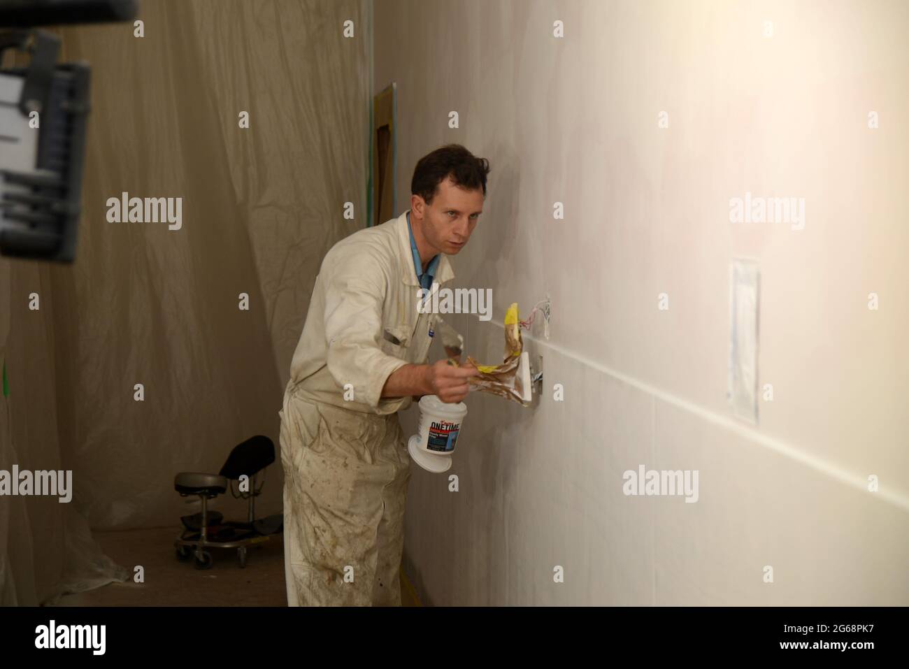 un commerçant regarde le long d'un mur, à la recherche de trous à remplir avant de peindre le manteau final Banque D'Images